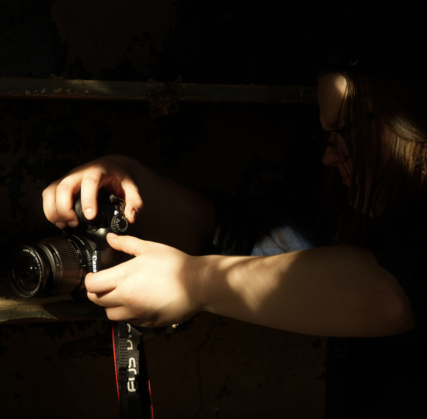 A woman adjusting a Canon camera in a dark, shadowy environment.
