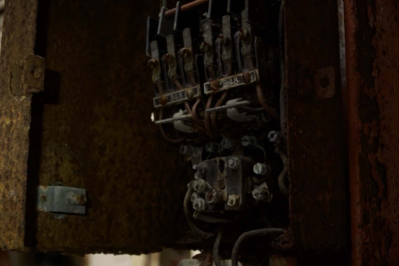 Close-up of an old, rusty electrical box with exposed wires and circuit breakers.
