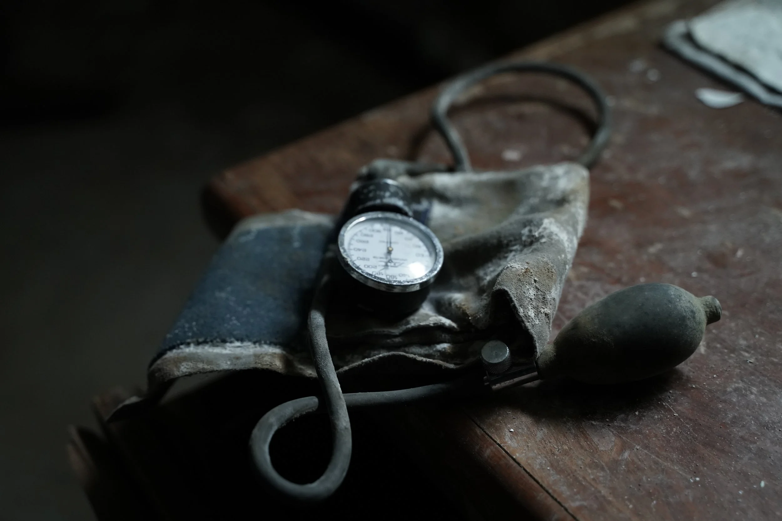 Close-up of a worn-out automotive part, possibly a brake caliper or smaller engine component, with a pressure gauge resting on a dirty, dusty wooden surface.