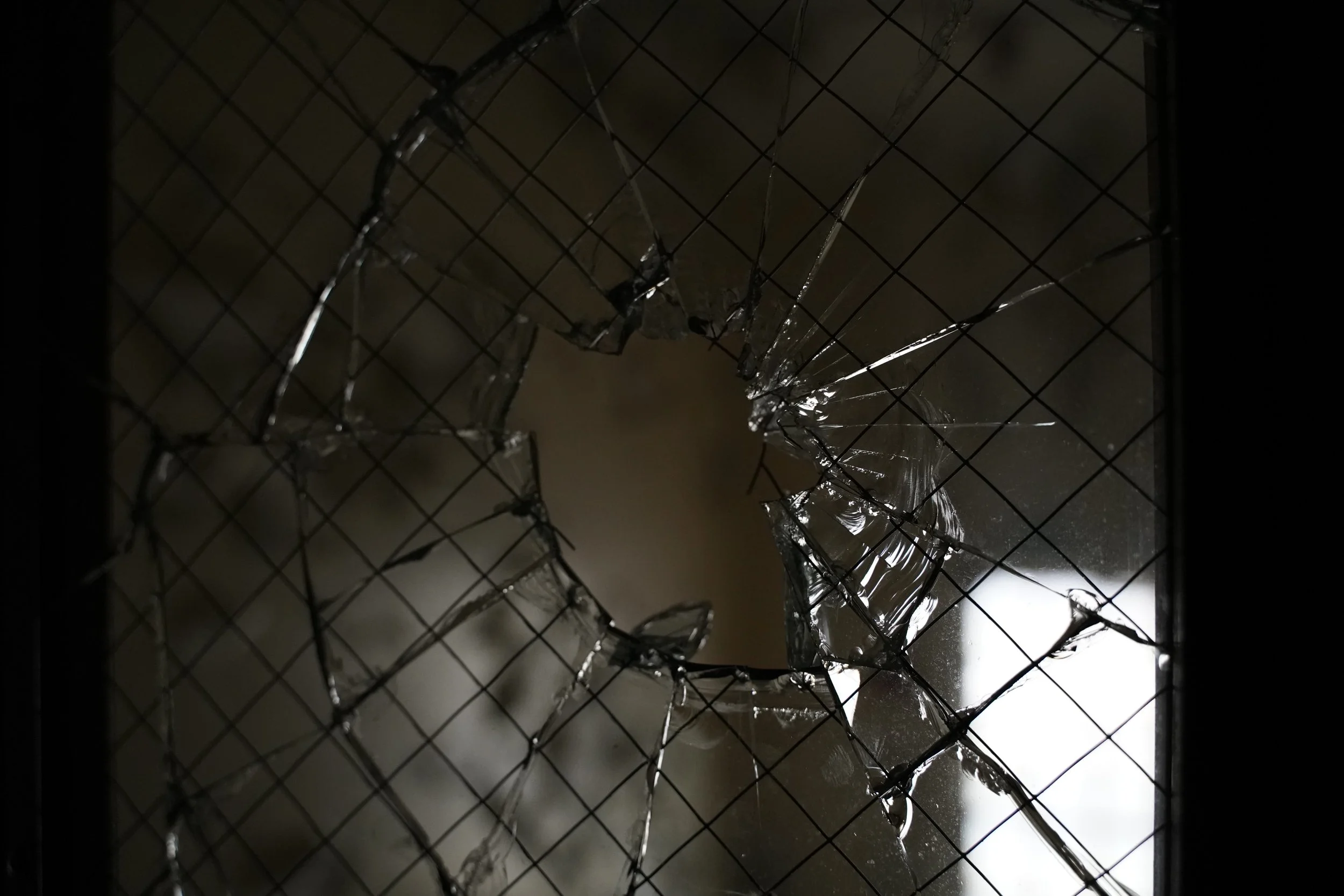 Shattered glass on a wire mesh surface with dark background and light reflection.
