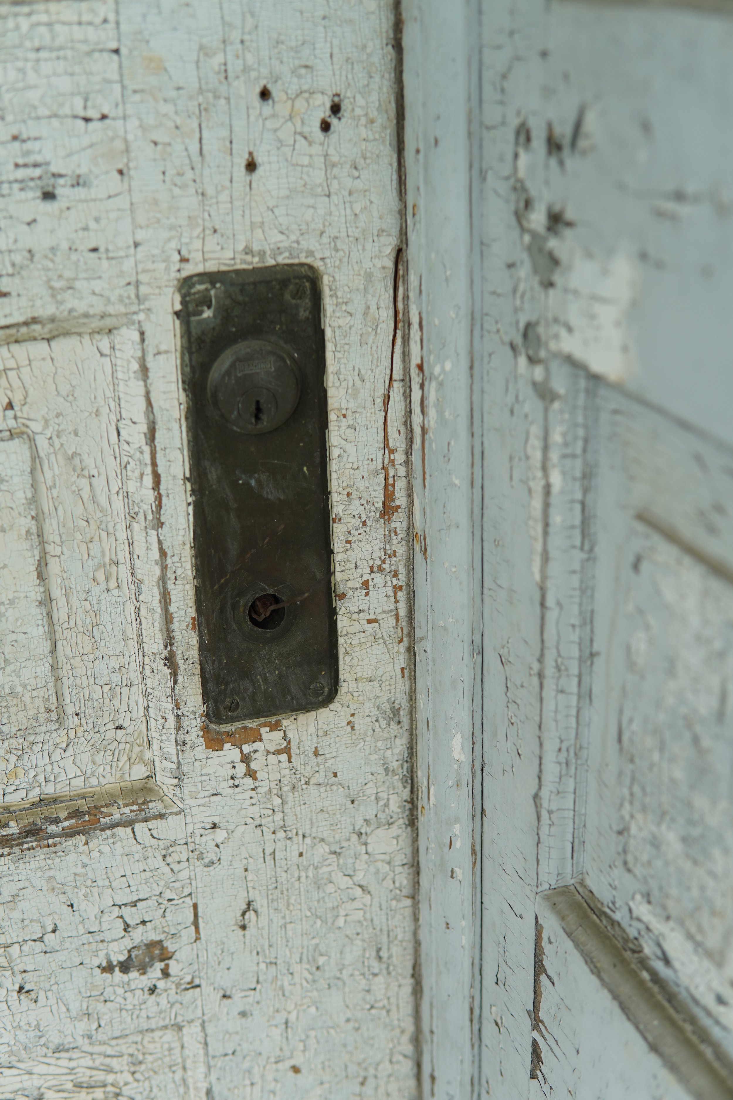 Close-up of a worn and peeling white-painted wooden door with an old, rusty, black metal lockplate.