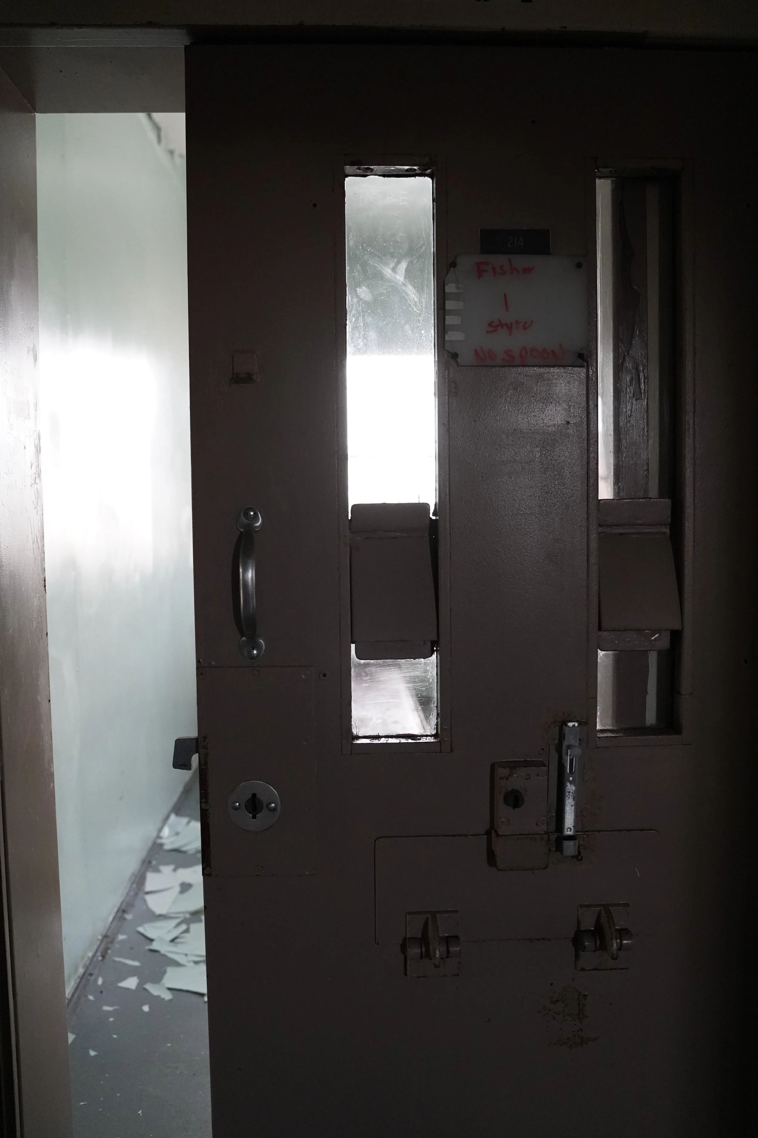 A dark, partially open metal safe door with writing on a white board attached to the wall, and damage visible inside and around the door.