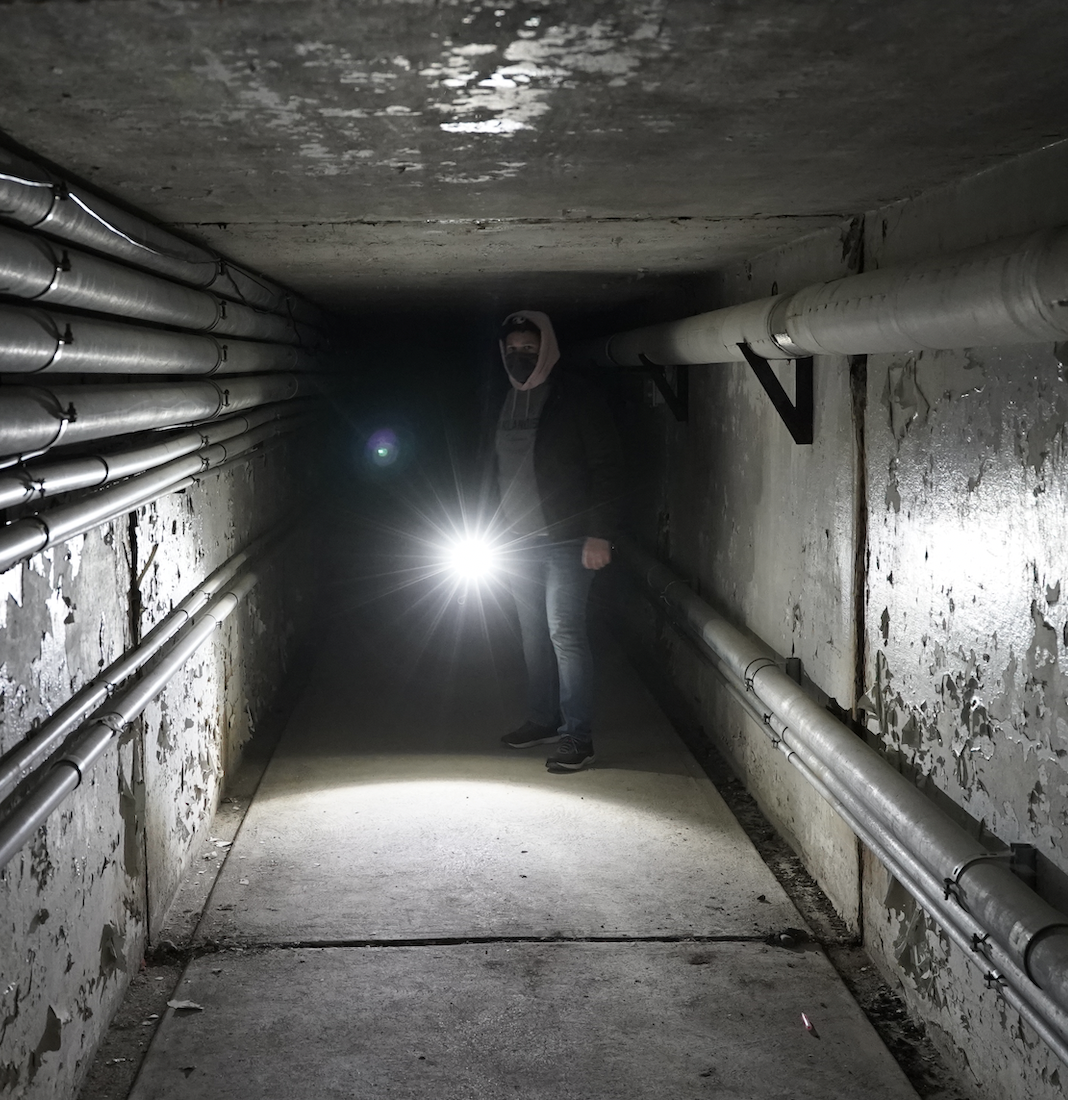 A man standing in a dark tunnel shining a flashlight at the camera.