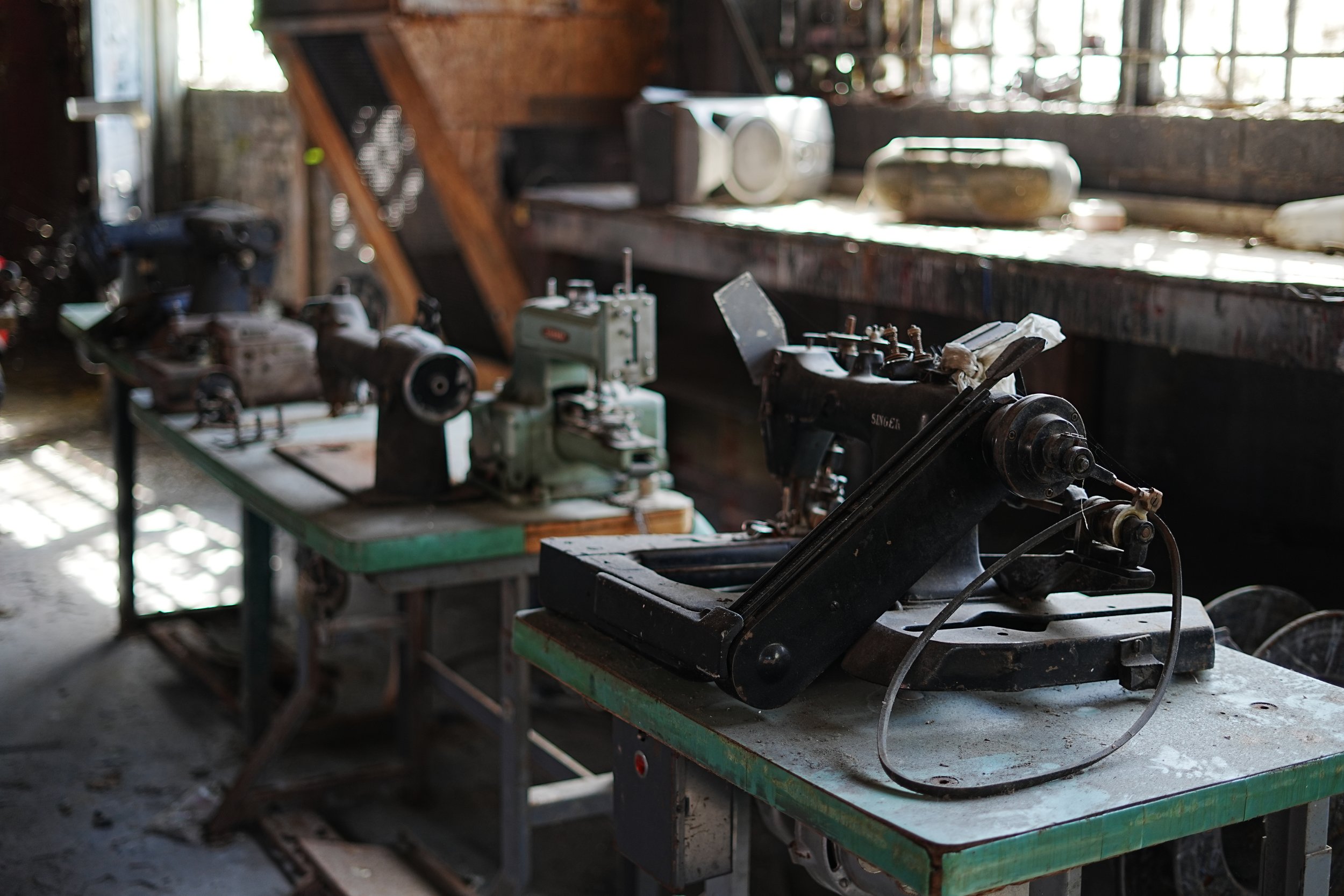 Old machinery and tools on workbenches in a rustic workshop with natural light coming through the window.