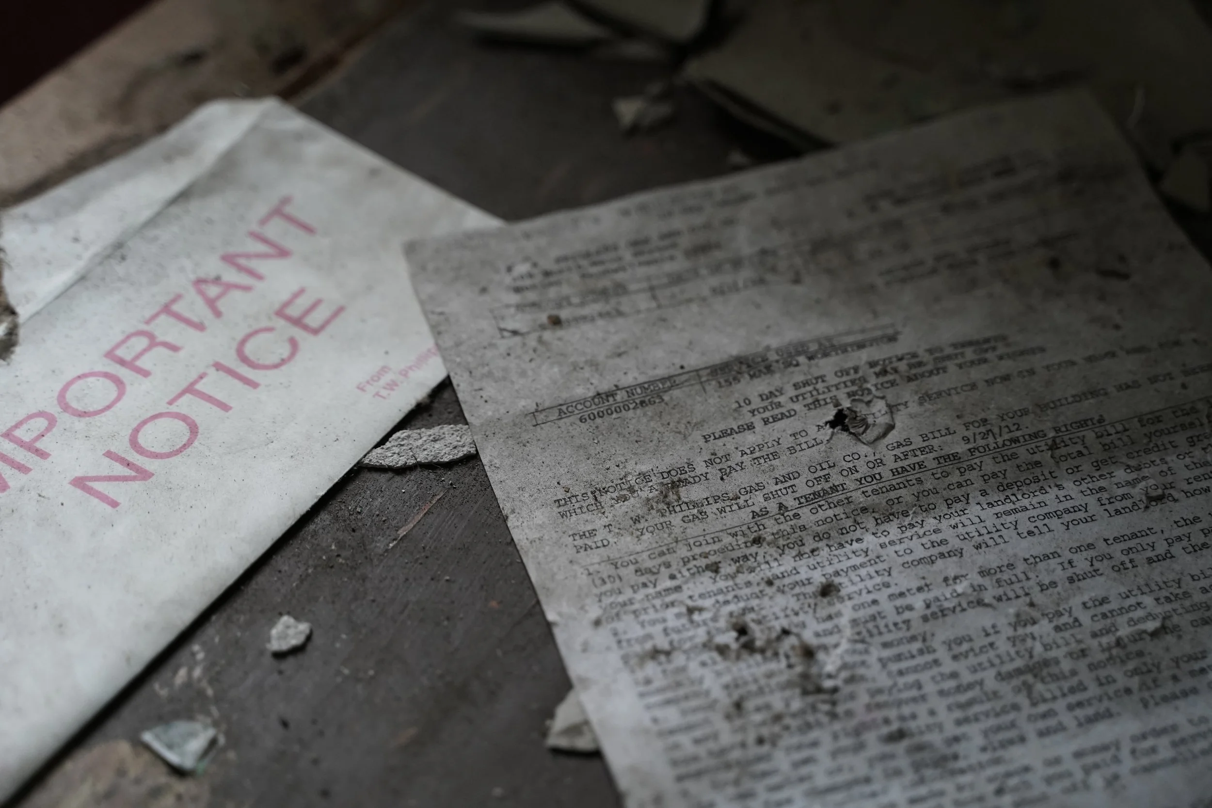Dirty, charred, and torn paper documents on a dusty surface, some with partially visible text and a warning label.