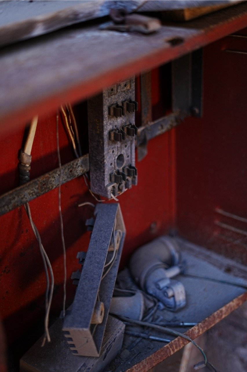 Close-up of an old, rusty mechanical device inside a red metal box, with some wires and a gray cloth at the bottom.
