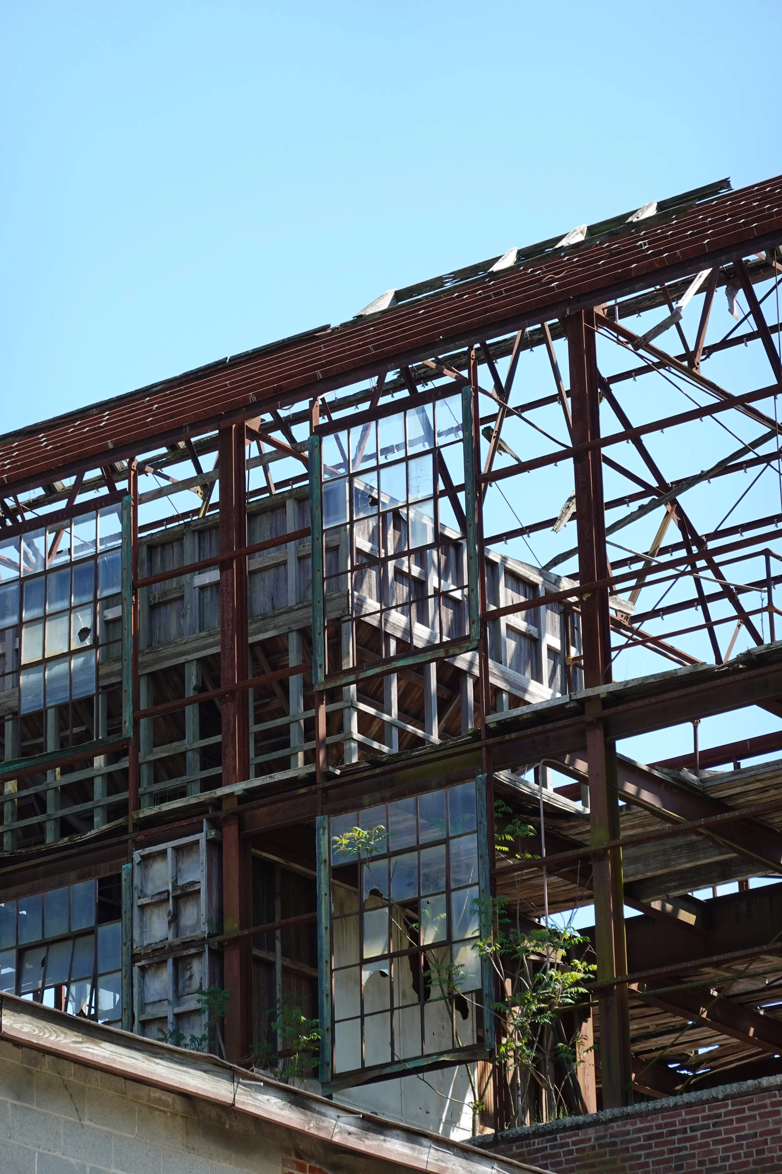 An old, abandoned building with a partly destroyed roof and broken windows, visible under a clear blue sky.