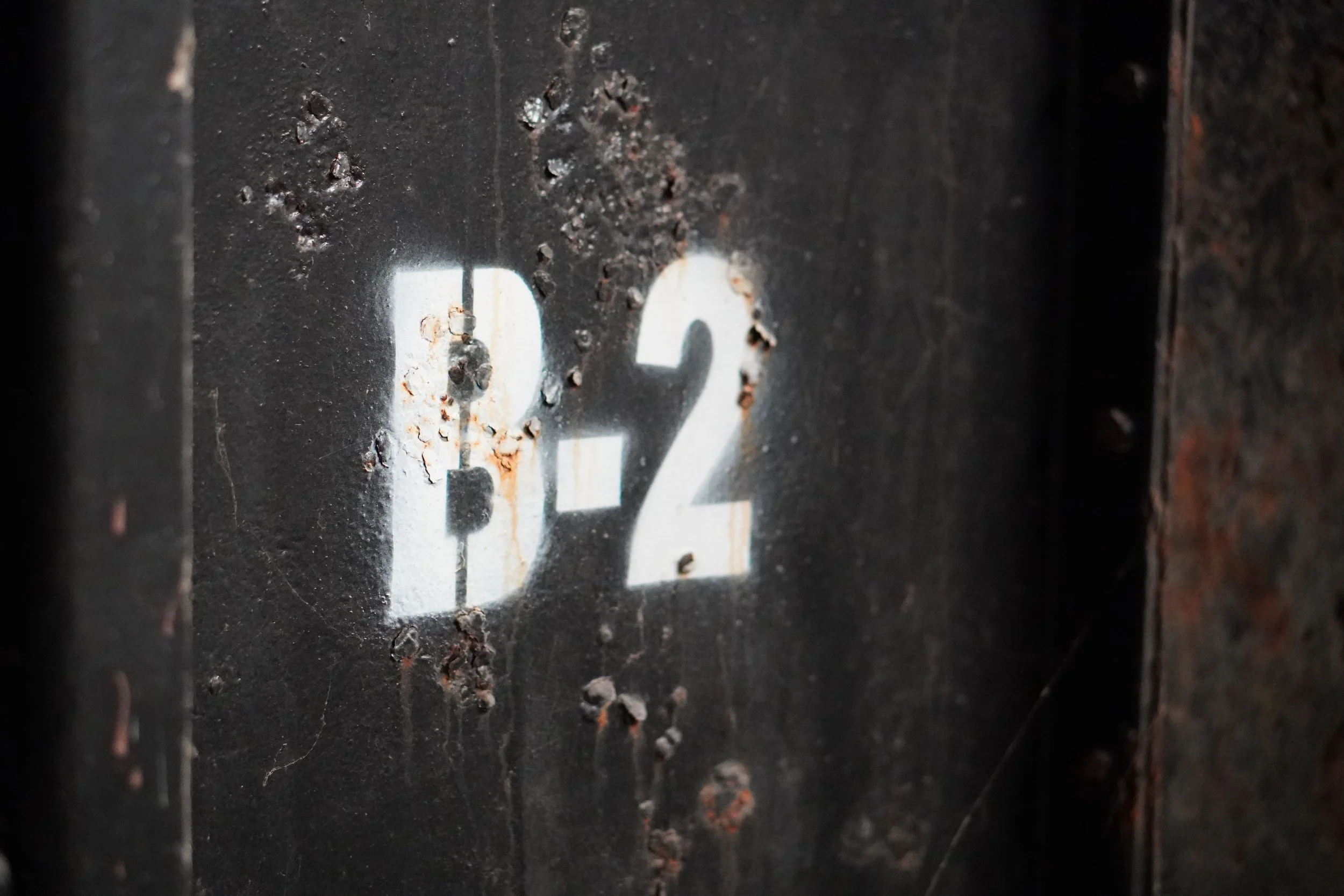 Close-up of a worn black metal surface with the number 92 painted in white, showing rust and chipped paint.