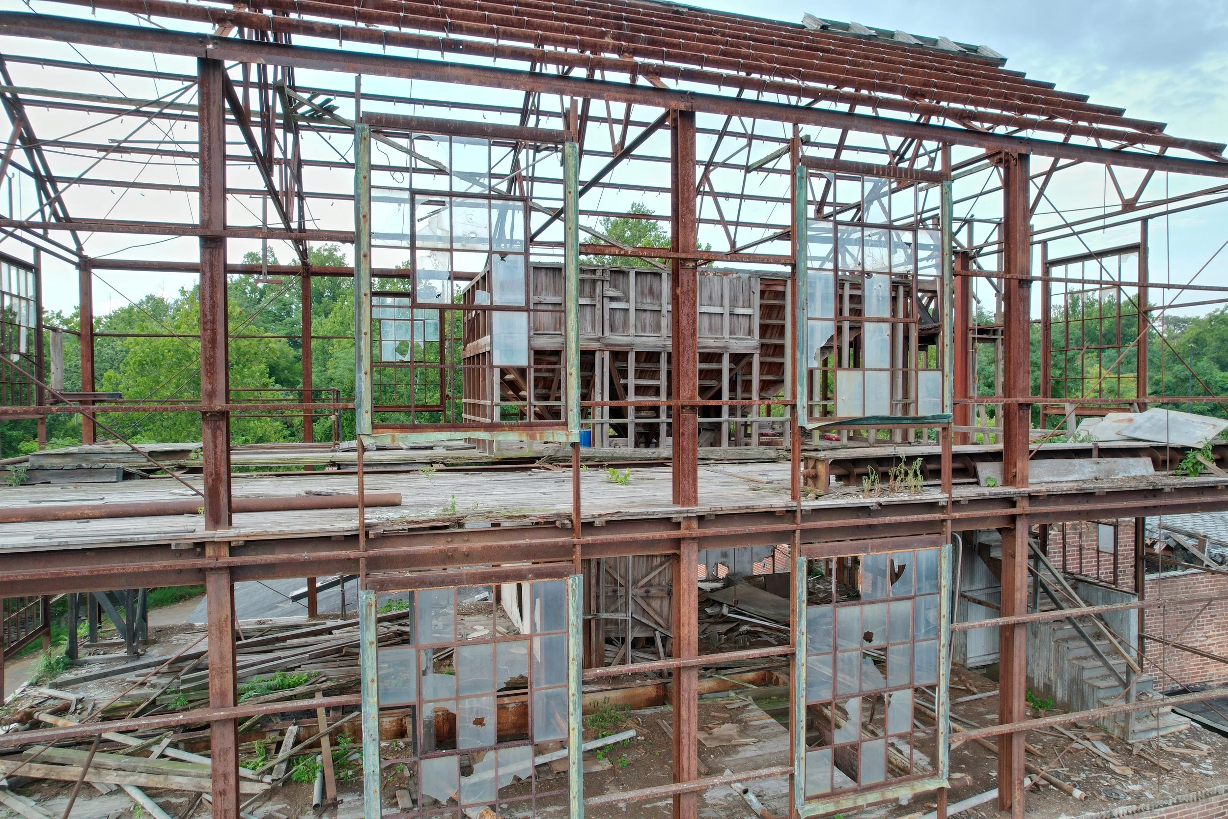 Ruined glass and metal structure of an abandoned building with broken windows and overgrown vegetation.