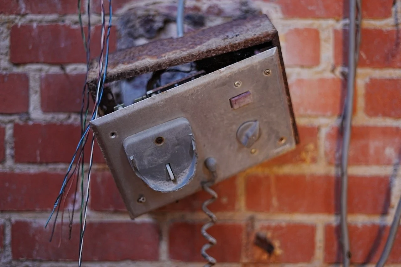 Old and rusty electric meter box mounted on a brick wall, with some wires hanging nearby.