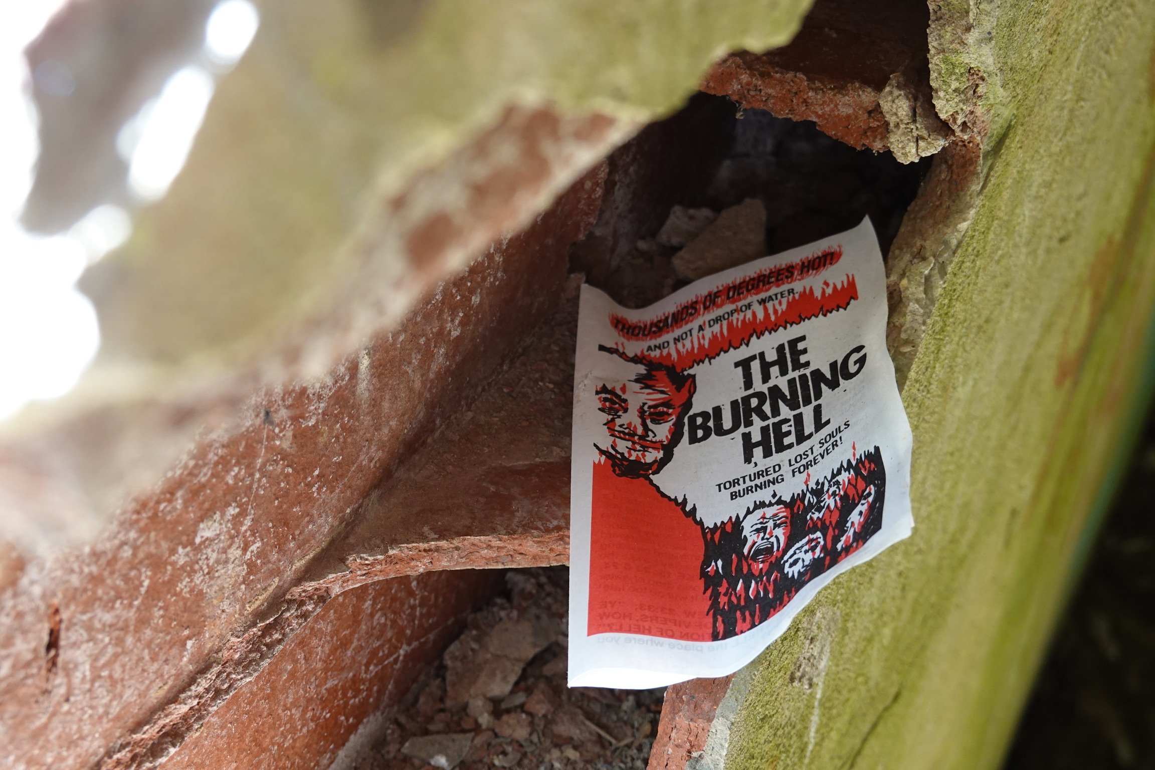 Close-up of a weathered brick wall with a torn protest poster that reads "The Burning Hell" and features an illustrated face of a person with flames around them.