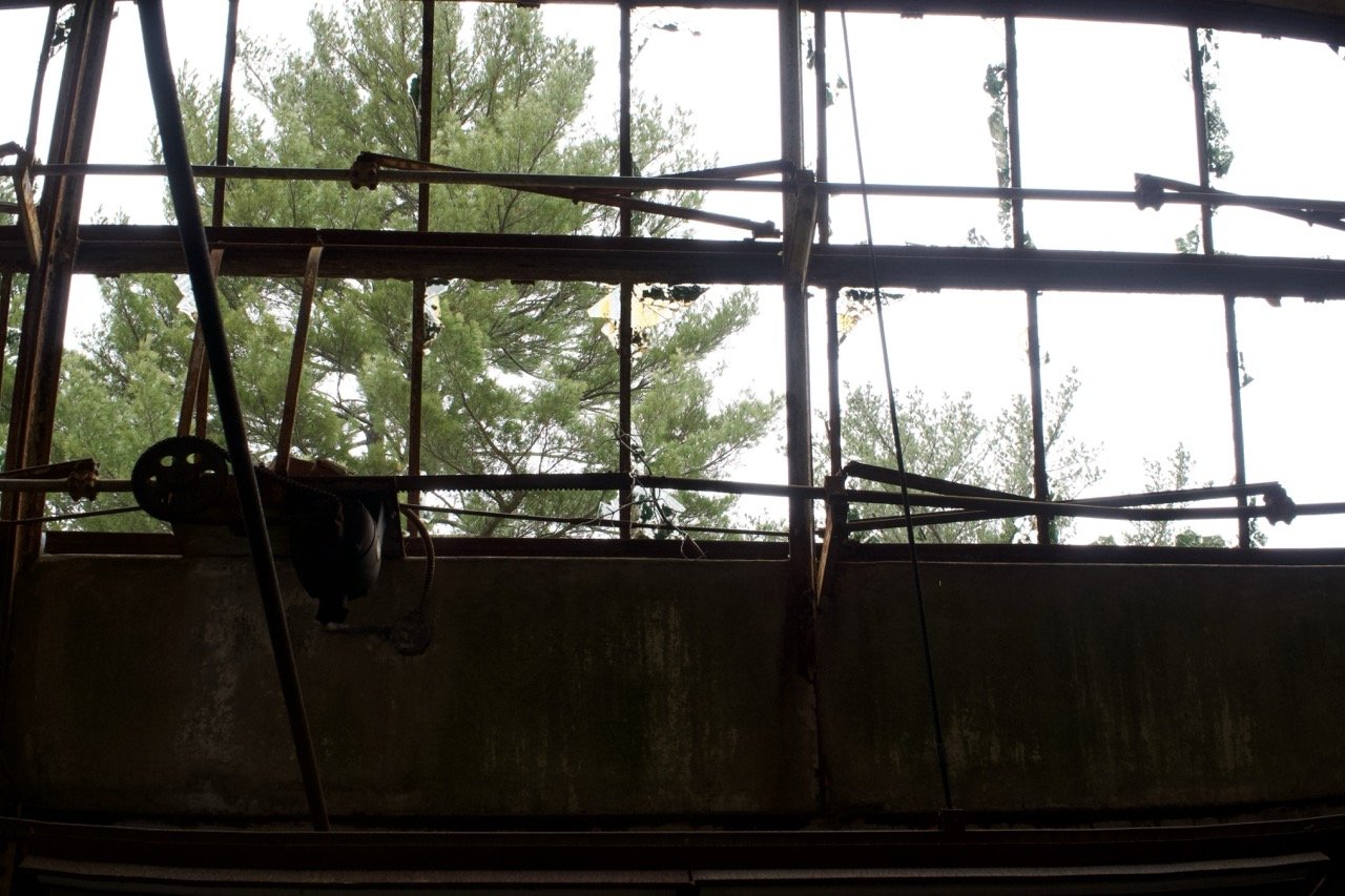View of a rusty, broken, windowless structure with trees and sky visible outside.