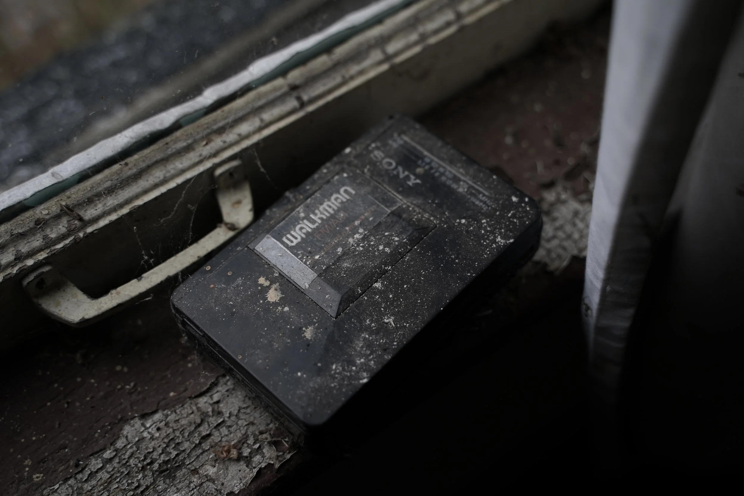 Close-up of a dirty, dusty black wireless access point device labeled 'NETGEAR' beneath a window with a dust-covered wall and ground.