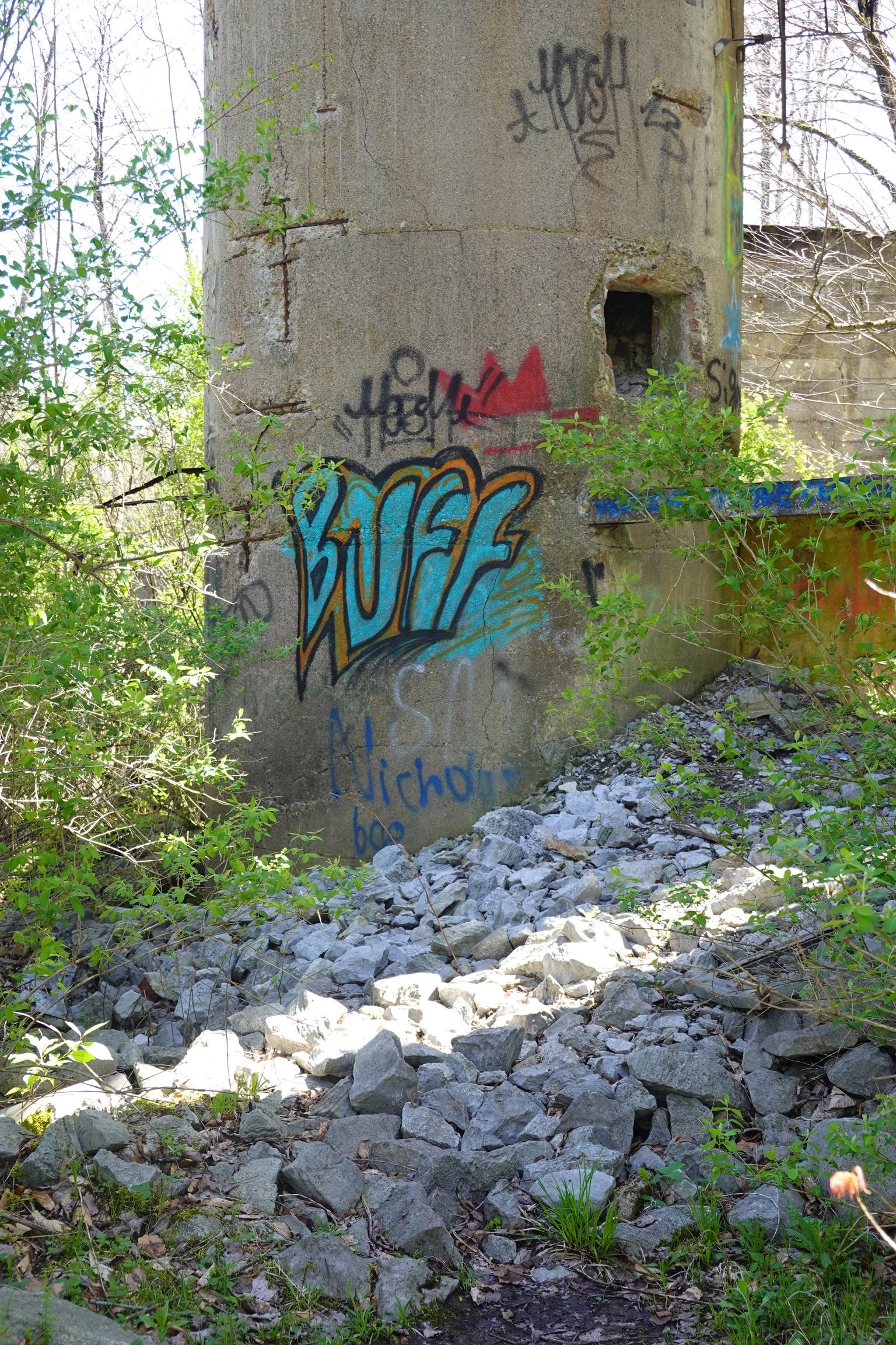 Concrete structure with graffiti, surrounded by greenery, rocks, and trees in the background.