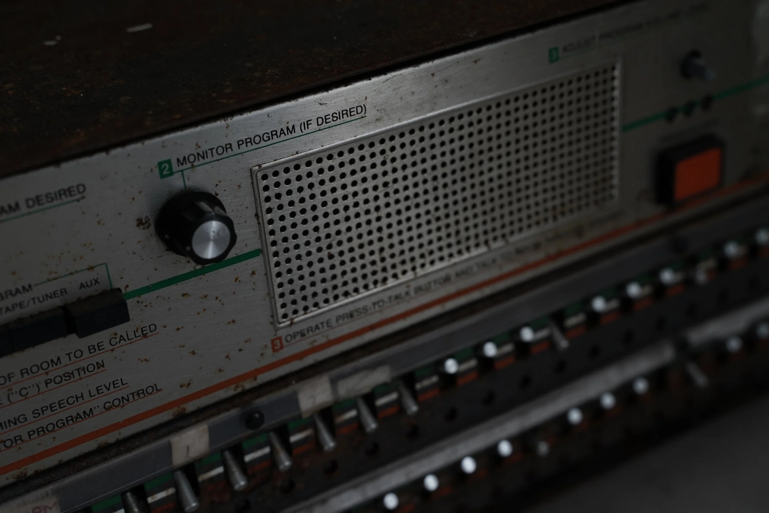 Close-up of a vintage electronic device with metal controls and a perforated panel, showing the words 'MONITOR PROGRAM (IF DESIRED)'.