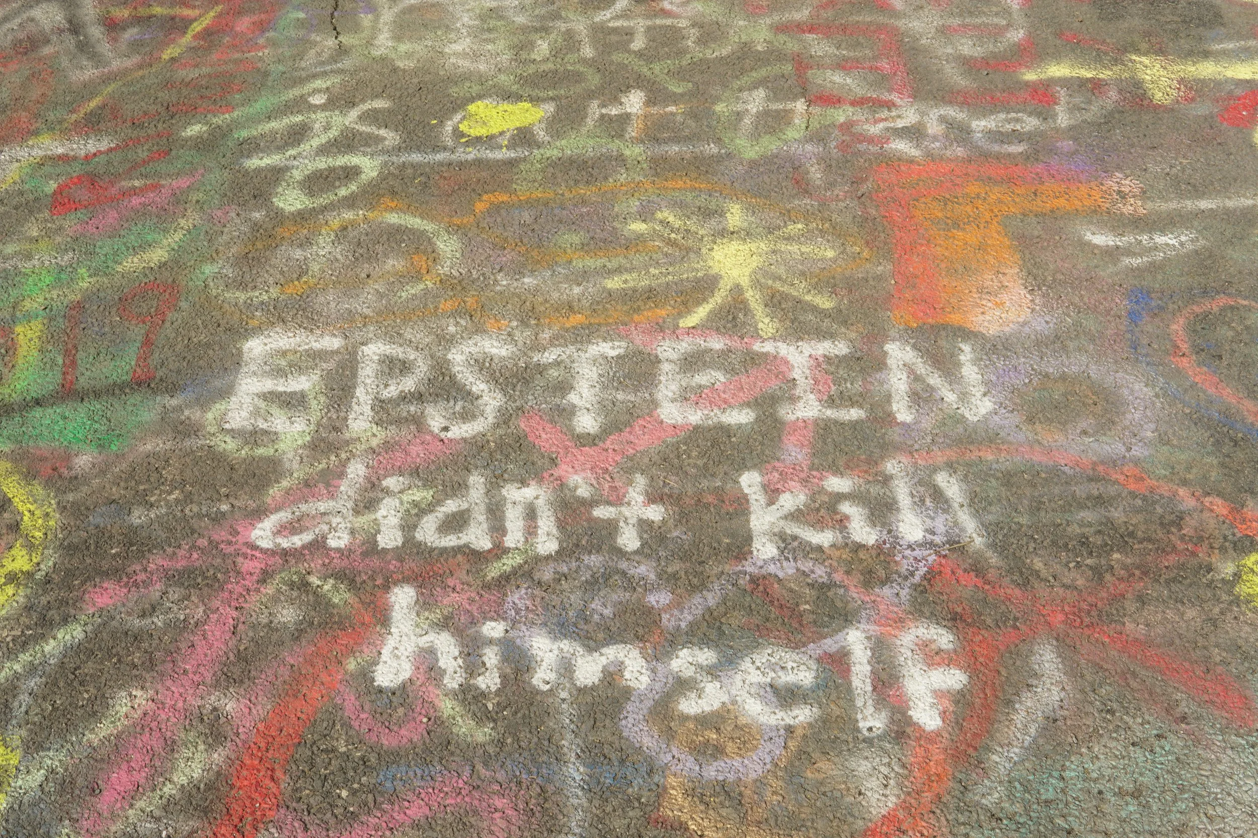 Colorful chalk drawings and writings on a concrete sidewalk, including a yellow butterfly, a red flower, and various multicolored shapes and words.