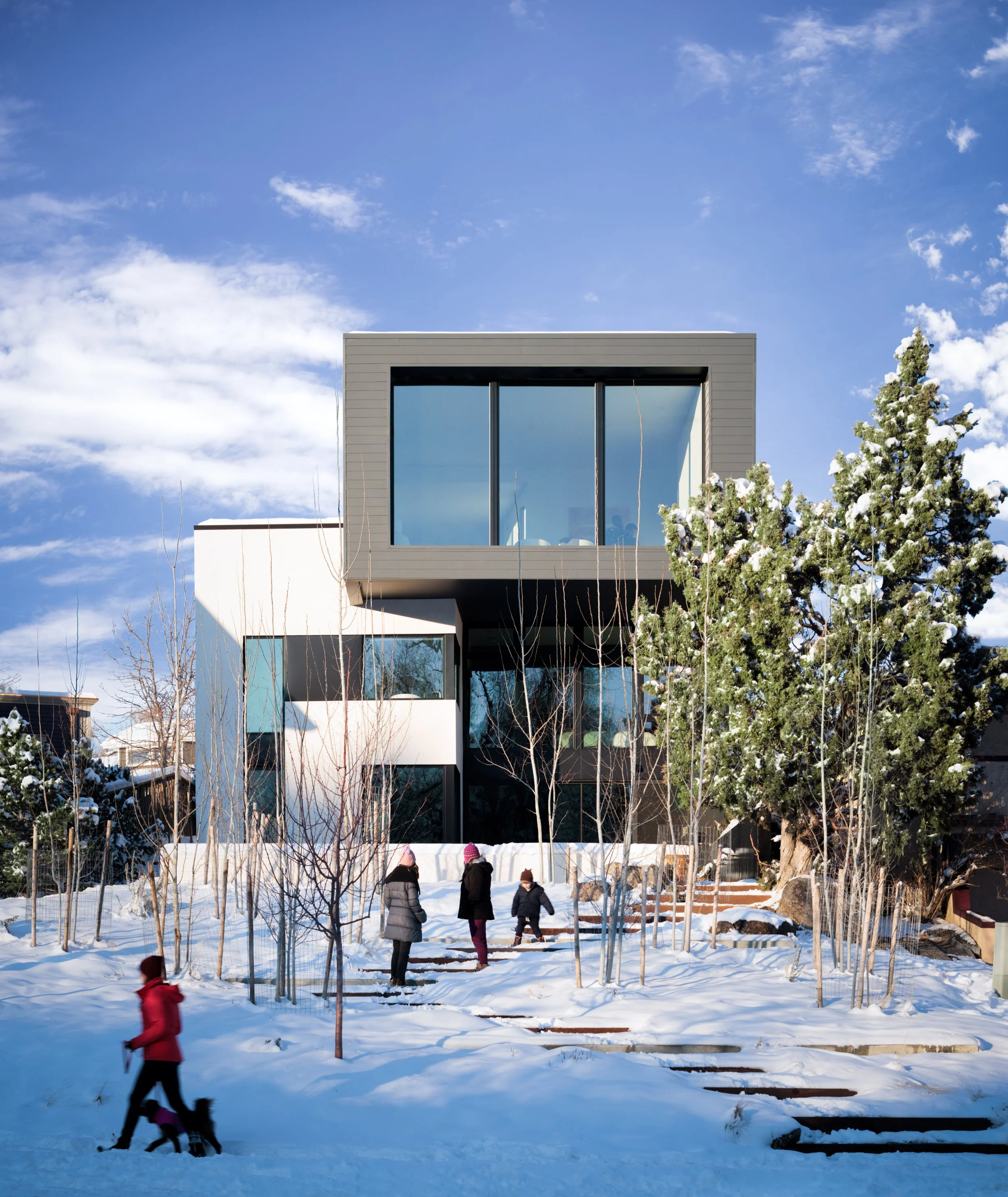 People walking in a snowy backyard with a modern house and snow-covered trees.