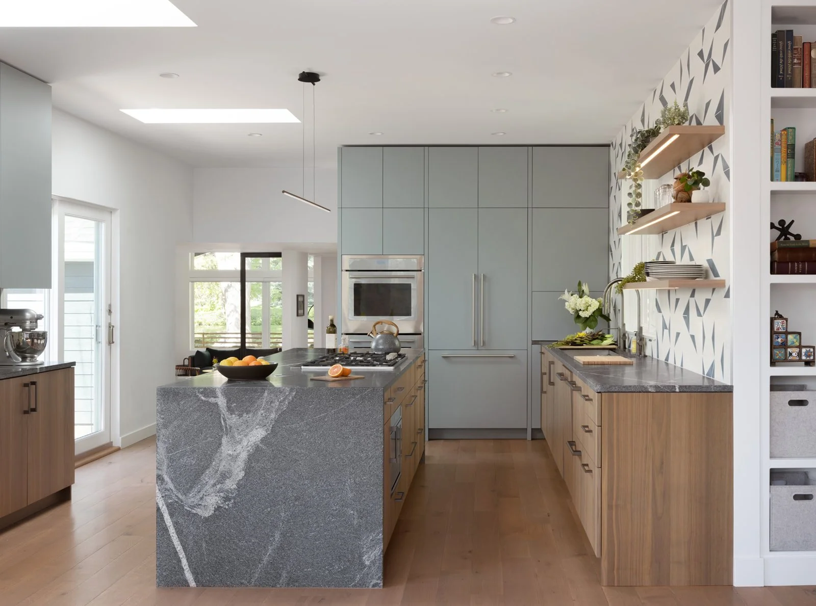 Modern kitchen with gray and wood cabinetry, a marble island, open shelving, and natural light from skylights and windows.