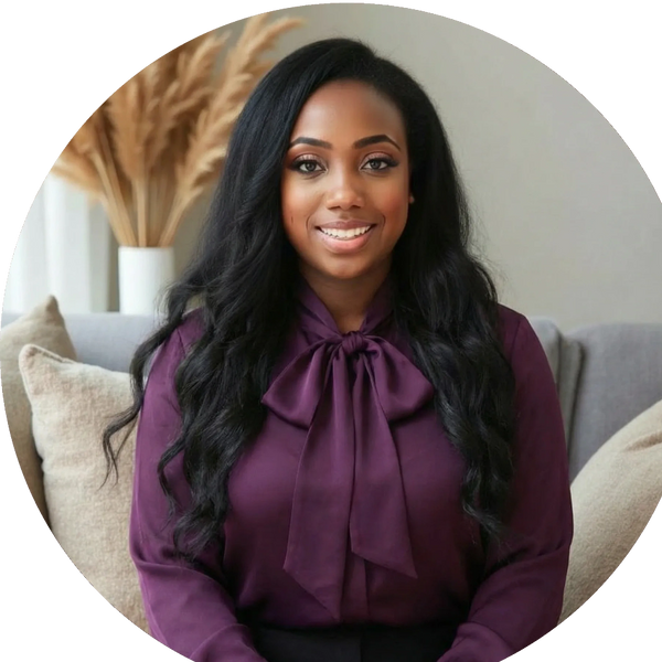 A young woman with long wavy black hair, wearing a purple blouse with a bow tie, sitting on a sofa with beige pillows in a modern living room.