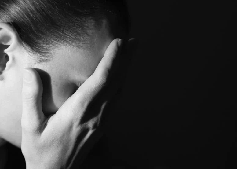 A person covering their face with their hand in a black and white photo.