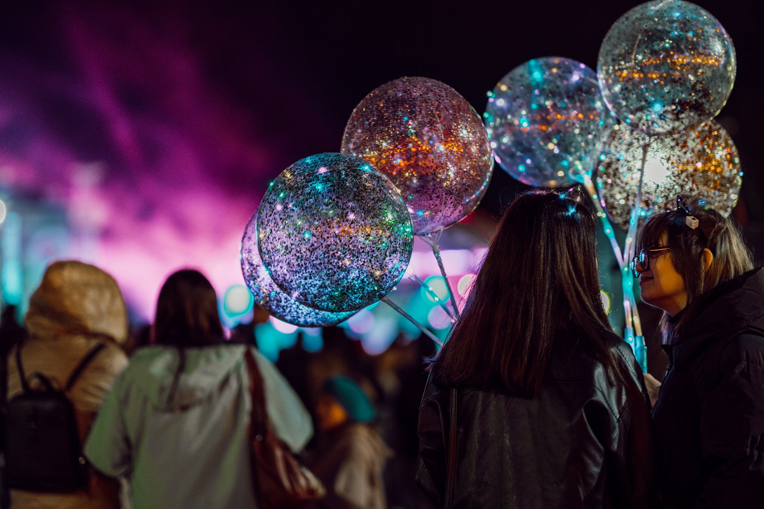 People holding illuminated, glittery helium balloons at night during a festival or celebration.