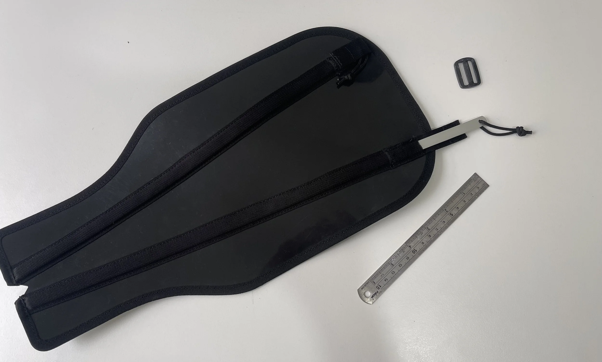 A black carrying case, a small rectangular buckle, and a stainless steel ruler are laid out on a white surface.