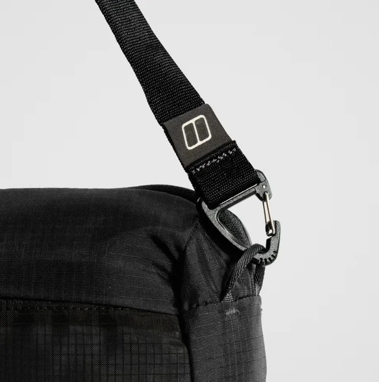 Close-up of a black bag with a strap and metal clip on a plain background.
