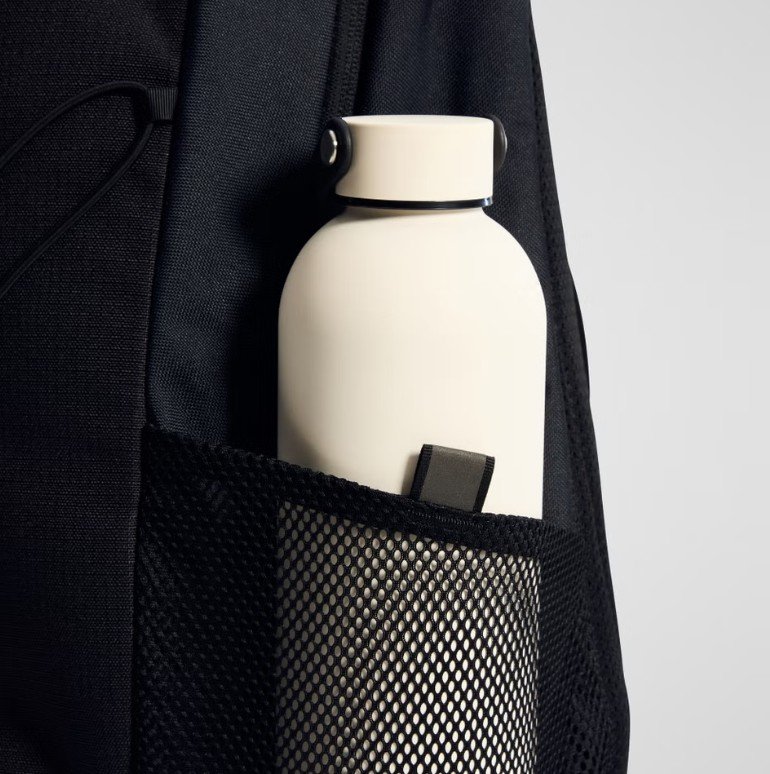 A white water bottle in the side pocket of a black backpack.