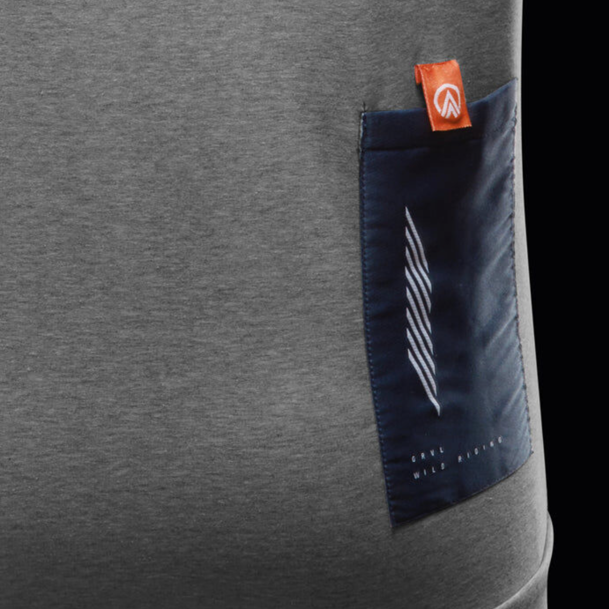 Close-up of a gray athletic shirt with a dark blue pocket on the side, featuring white diagonal stripes and small text reading "GRANDE WILD RANGER." A small orange tag with a white logo is attached to the top of the pocket.