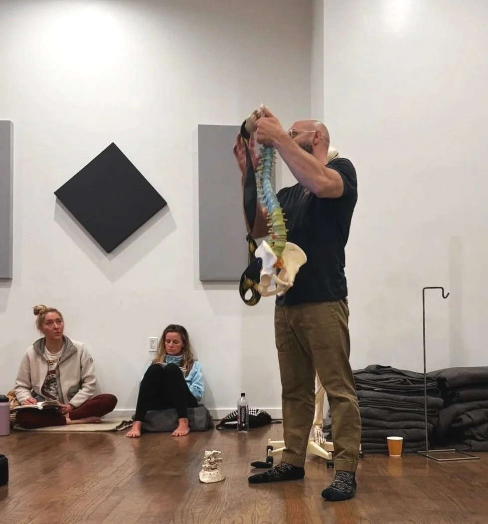 Chiropractor, Dr. Jeremy Brooks holding a human spine model in front of a group of seated students in a classroom or lecture setting.