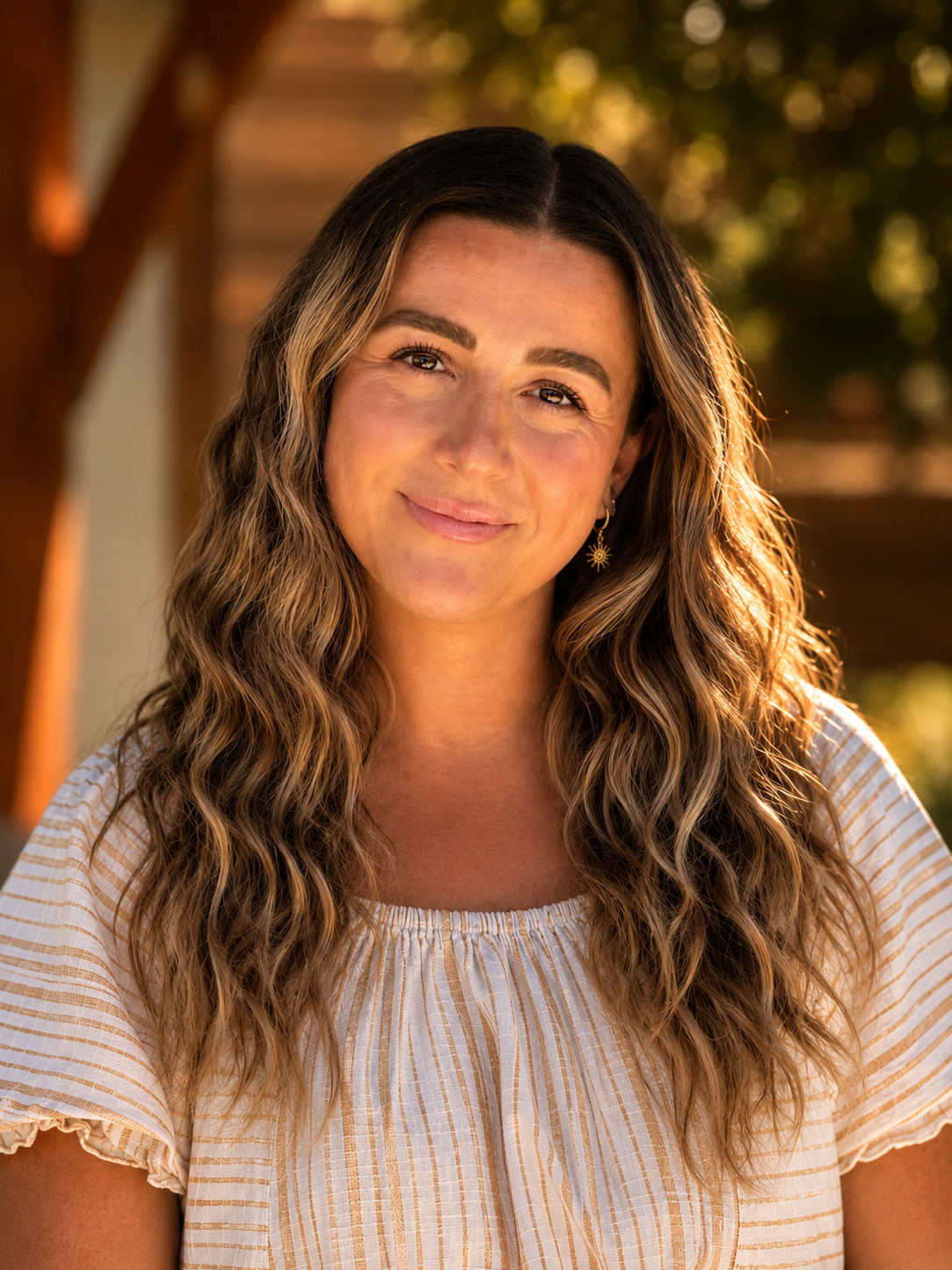 A woman with shoulder-length wavy hair, smiling, wearing a white blouse and a necklace, is pictured against a blue and gray geometric background.
