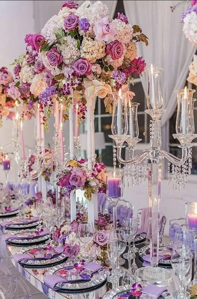 Elegant banquet table decorated with pink and purple floral arrangements, crystal candleholders with lit candles, and fine glassware and tableware for a formal event.