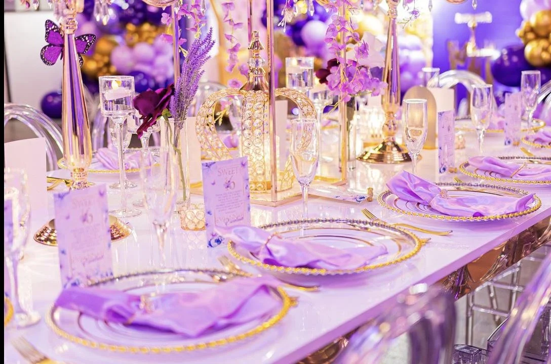 Decorated banquet table with purple and gold accents, floral centerpieces, candles, and elegant tableware at a celebration or wedding reception