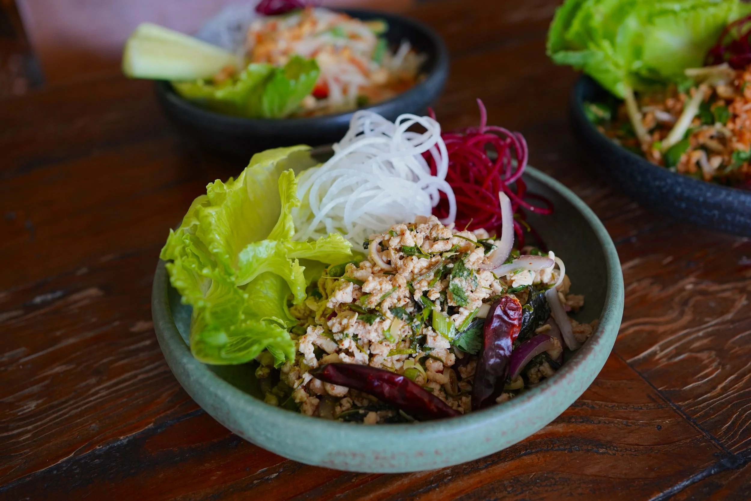 A bowl of fresh Larb salad with ground meat and herbs, garnished with lettuce leaves, on a rustic wooden table.