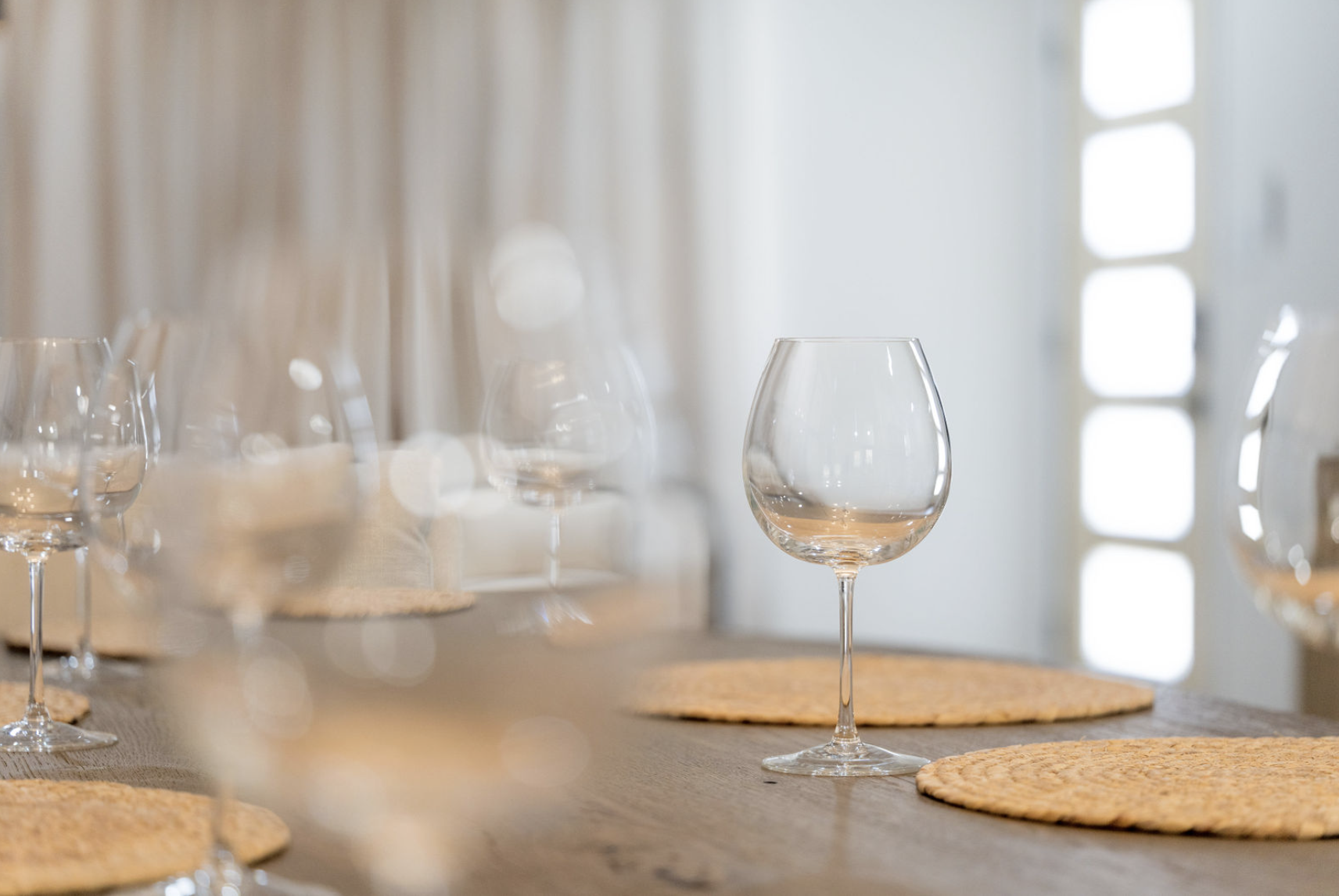 Empty wine glasses on a dining table with woven placemats, set with natural light from a window.