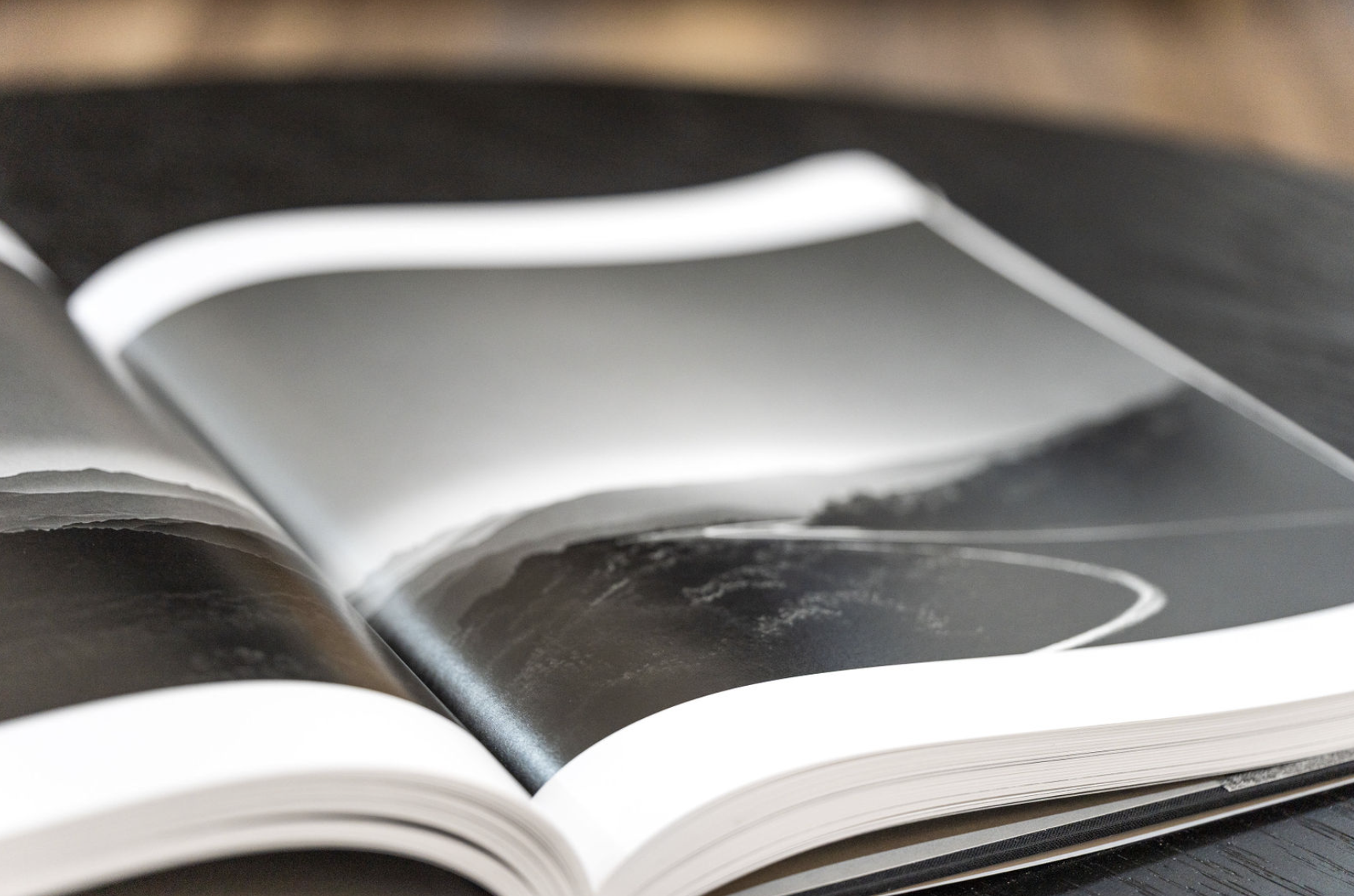 Close-up of an open magazine displaying black and white abstract images on glossy pages, resting on a dark wooden surface.