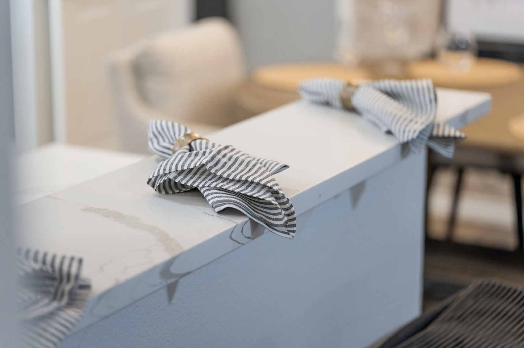 Two striped napkins with gold rings tied around them, placed on a white countertop, in a dining or restaurant setting.