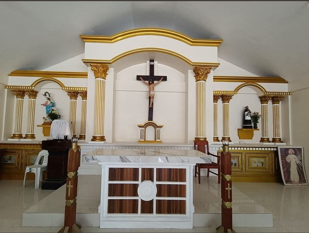 Interior view of a church altar with a crucifix, statues of saints, and gold accents.
