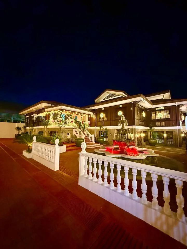 Night view of a well-lit, two-story house with a fountain in the front yard, decorated with Christmas lights and ornaments.