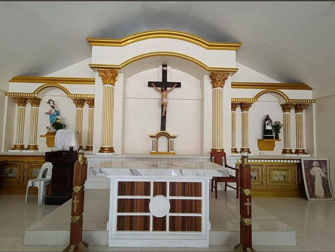 Inside a church, altar with crucifix, statues of religious figures, and gold decorative columns and arches.