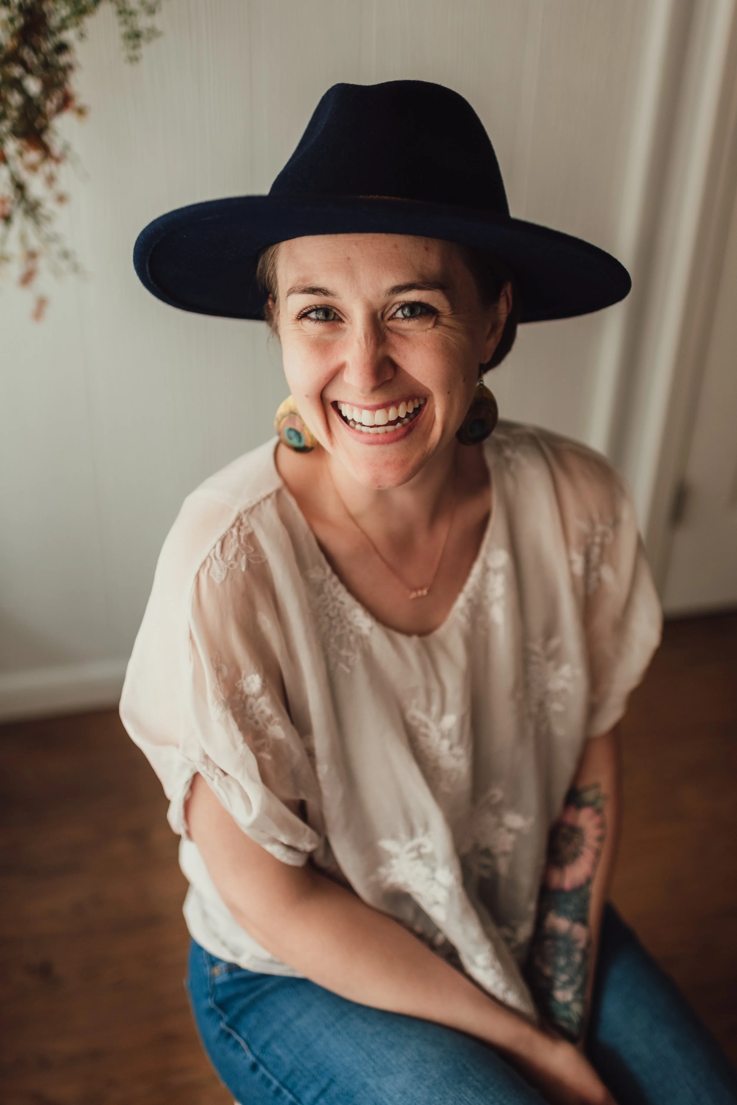 A woman, Eralore Studio's founder Ashley Snow, sits with a wide brim hat and a big smile.