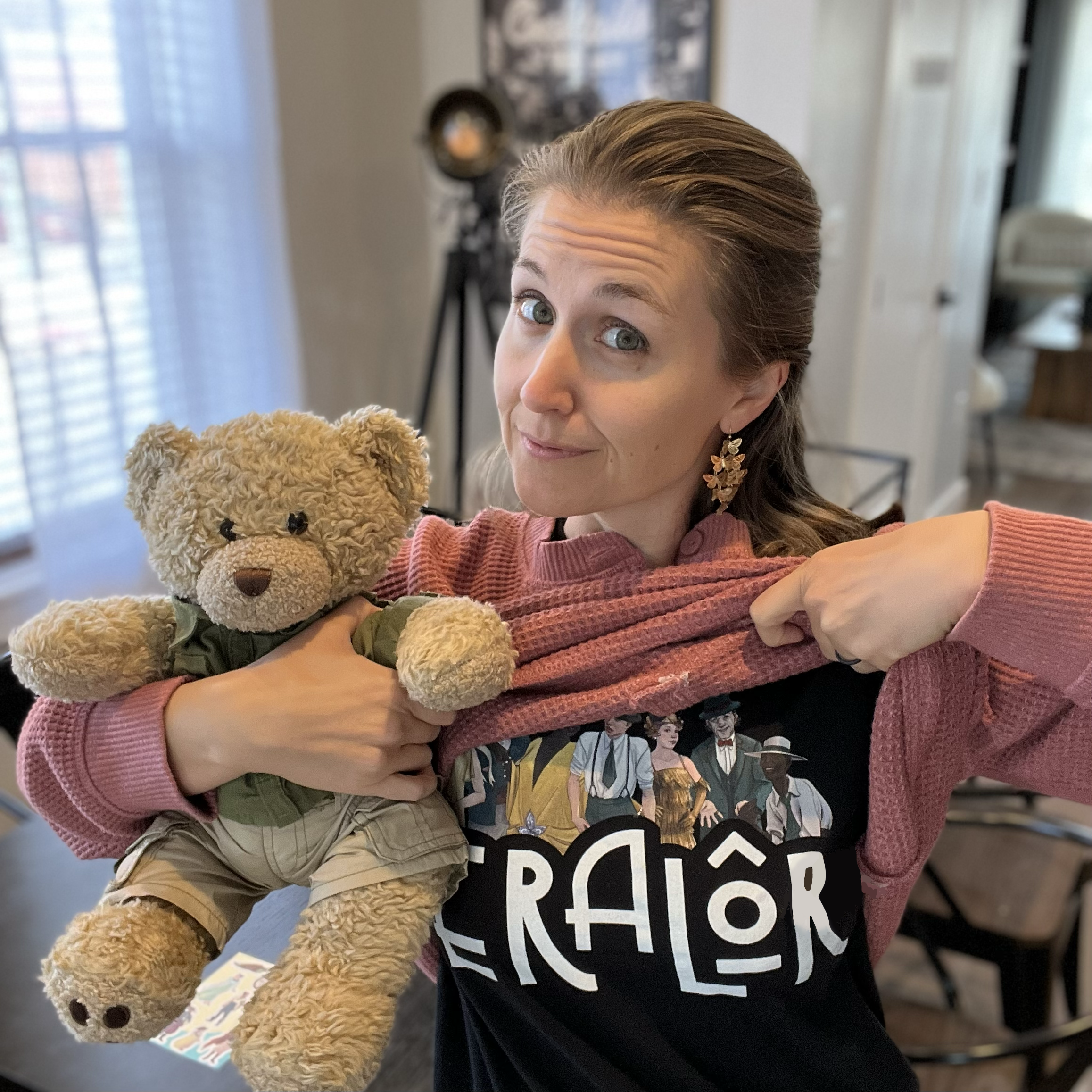Ashley, founder of Eralore, lifts her shirt to reveal an Eralore themed shirt beneath, while holding her teddy bear.
