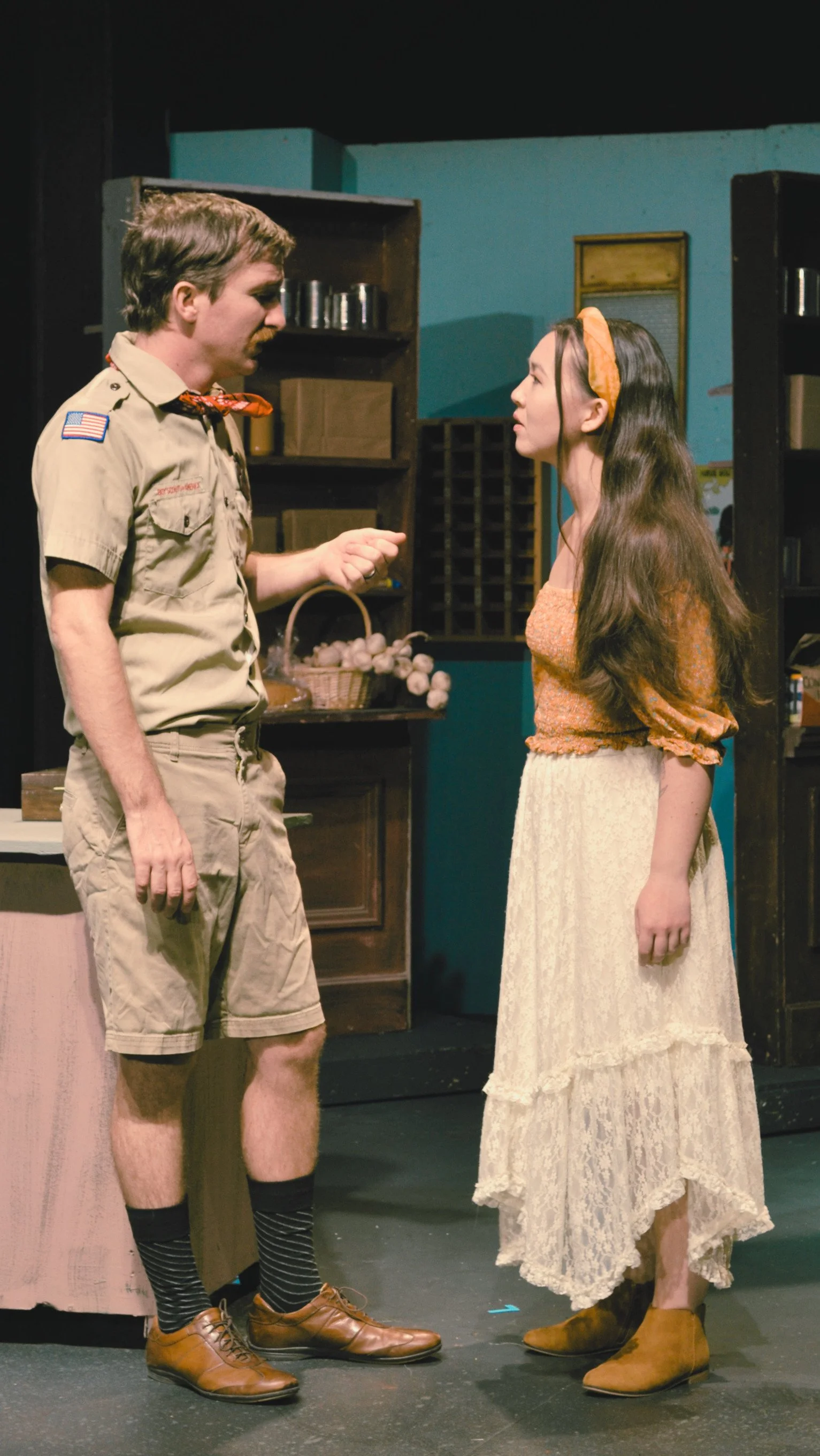 A man dressed as a Boy Scout has a deep emotional conversation with a young hippie woman.