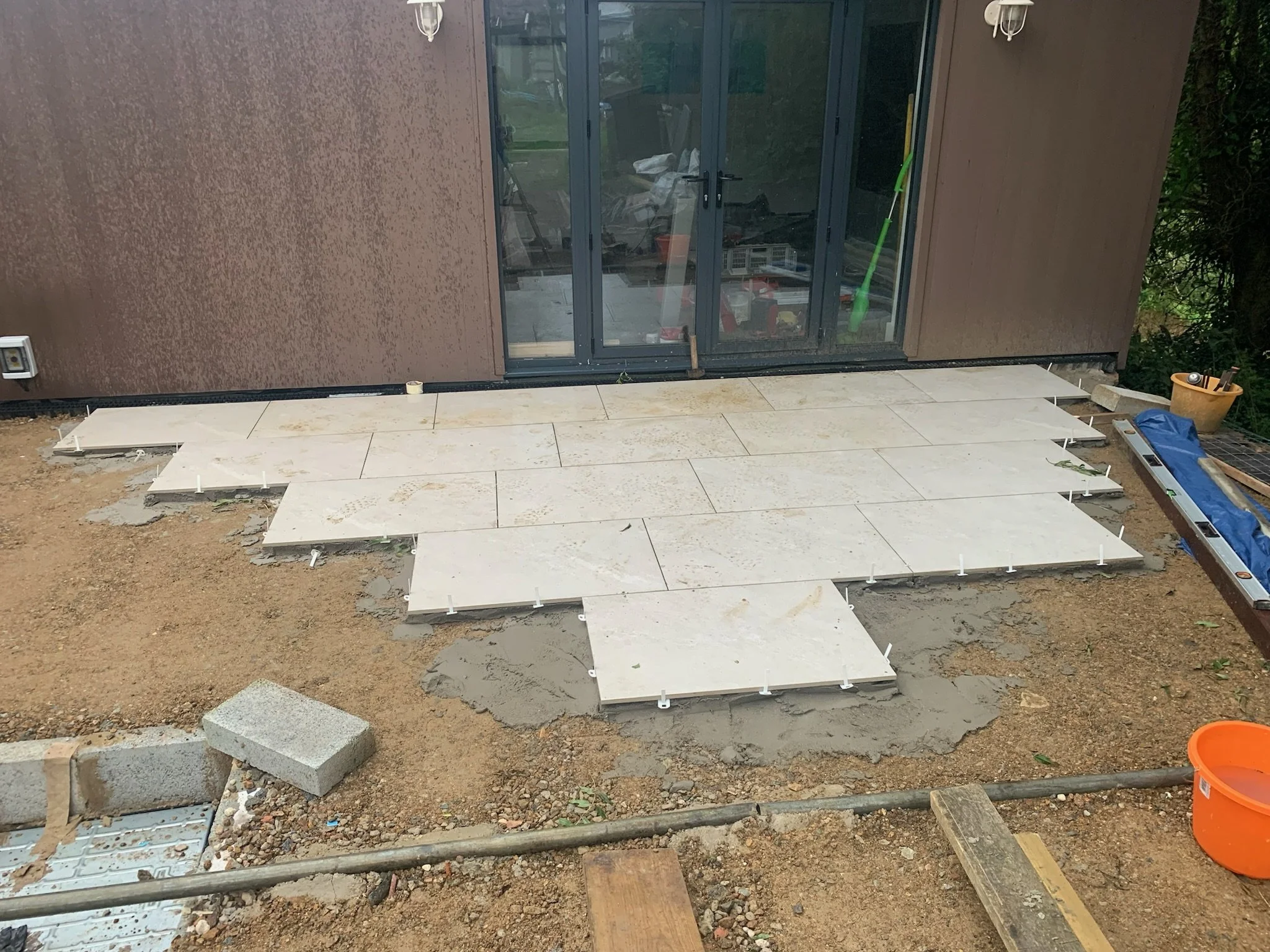 Construction site with newly laid stone tiles, tools, and materials for outdoor patio or walkway installation.