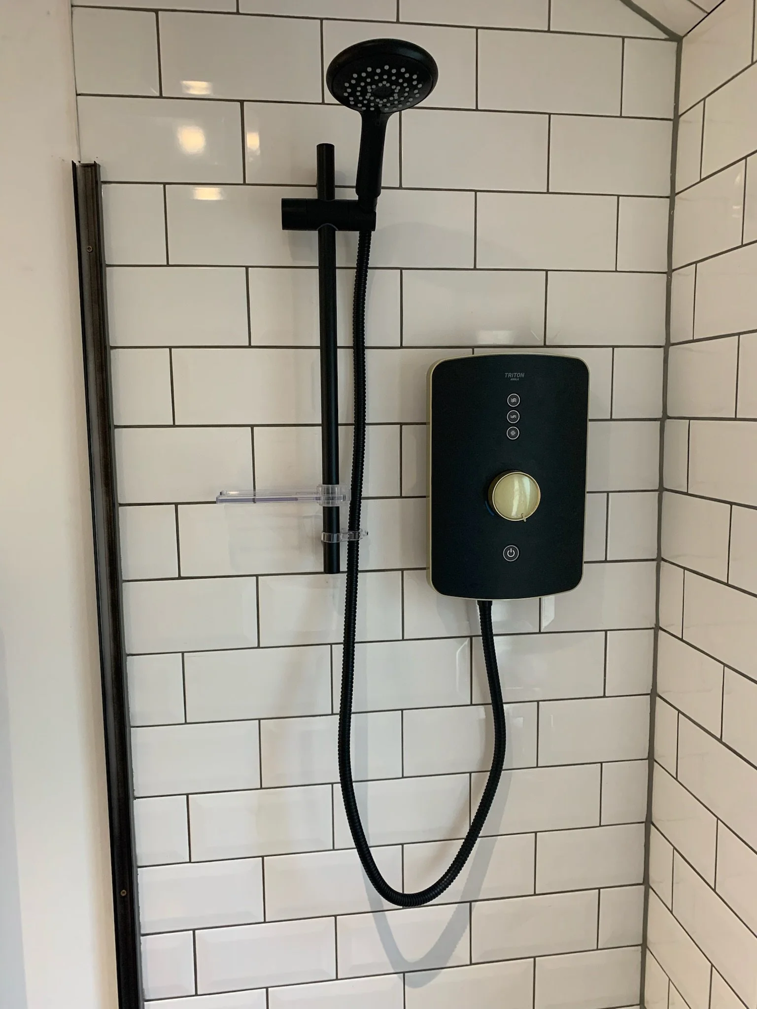 Shower head and control panel mounted on white subway tile wall in a shower stall.