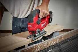 Guernsey Handyman using a cordless Milwaukee jigsaw to cut wood on a workbench.