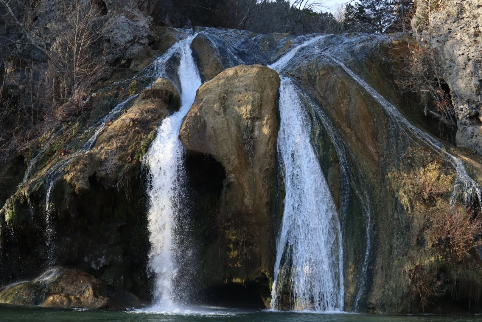 Waterfall cascading over rocks and cliffs surrounded by trees.