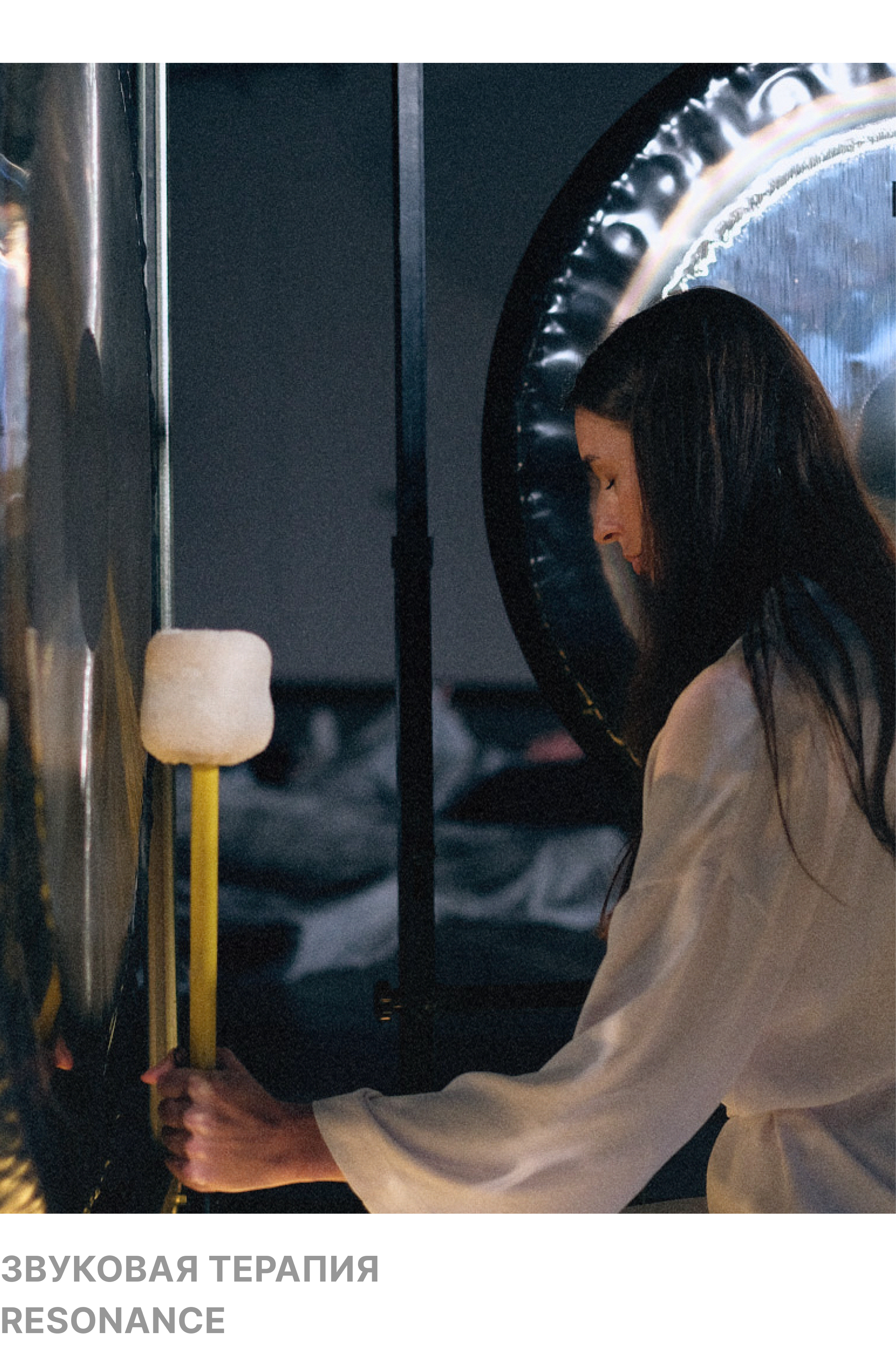 A woman with long dark hair is pressing a large button or switch on a wall, with her head bowed down and eyes closed, in a dimly lit room.