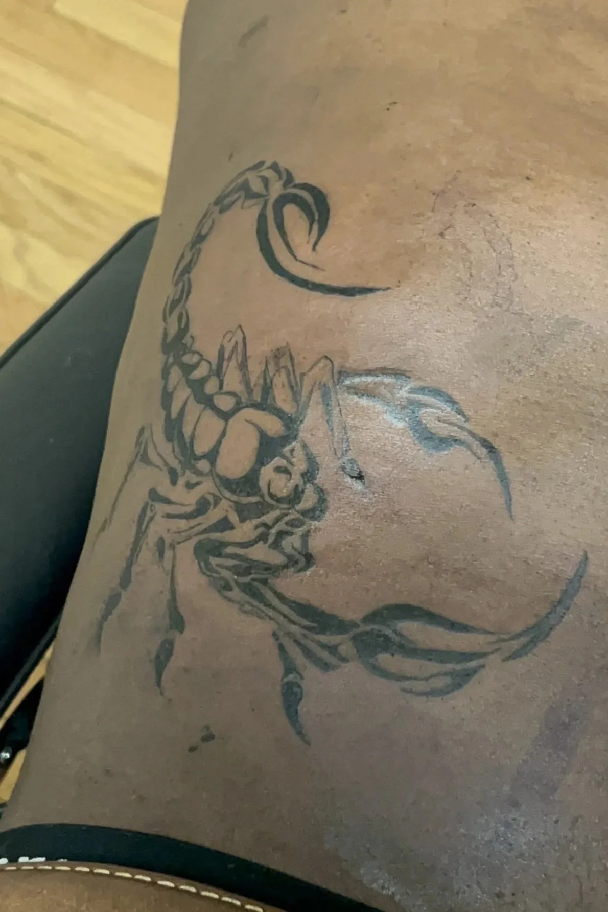 Tattoo of a scorpion in black ink on a person's leg, with the tail curled upward and claws extended.