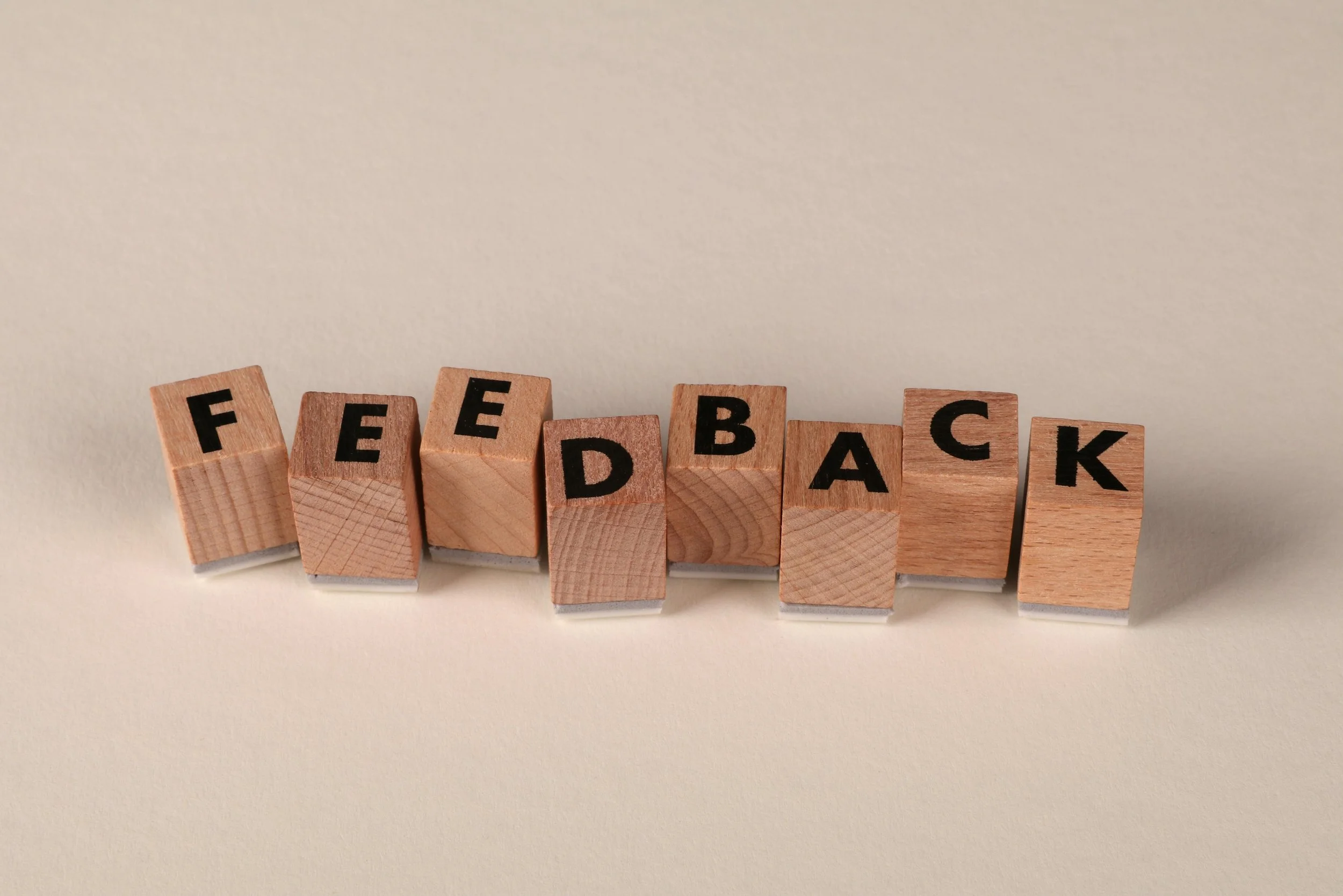 Wooden blocks spelling 'FEEDBACK' arranged in a line on a white surface against a plain background.